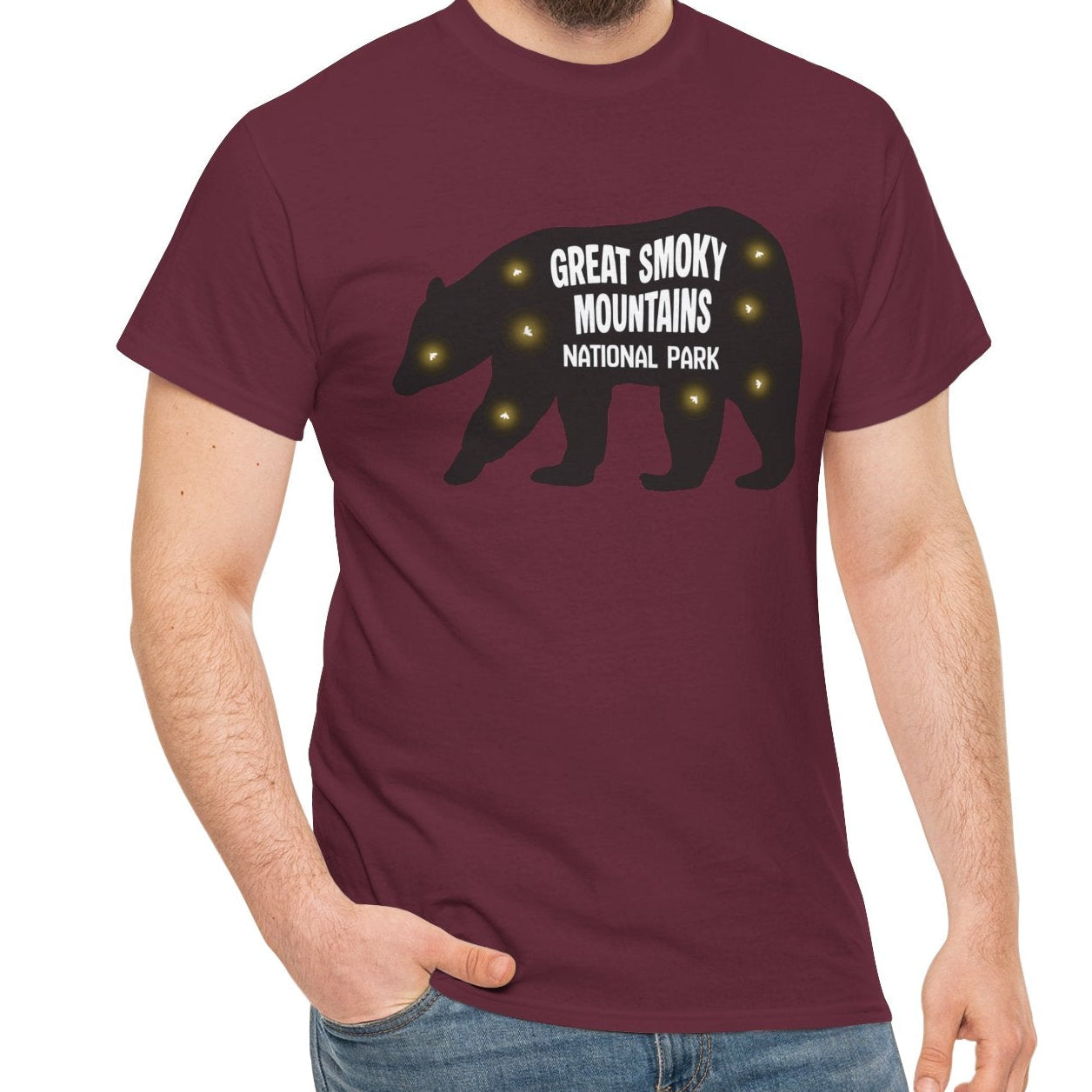 A man wearing a maroon short-sleeve t-shirt with a black bear silhouette and the text 'GREAT SMOKY MOUNTAINS NATIONAL PARK' with fireflies, paired with blue jeans, against a plain white background.