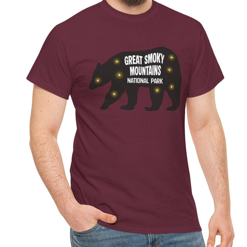 A man wearing a maroon short-sleeve t-shirt with a black bear silhouette and the text 'GREAT SMOKY MOUNTAINS NATIONAL PARK' with fireflies, paired with blue jeans, against a plain white background.