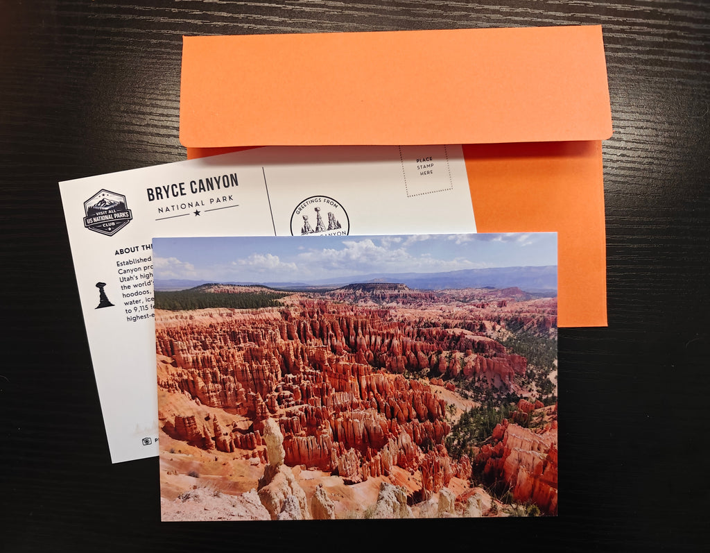 A postcard featuring a scenic photograph of Bryce Canyon National Park, displayed with an orange envelope on a dark wood background.